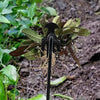 A black multifunctional hand weeder tool with a curved blade is shown in a garden setting.