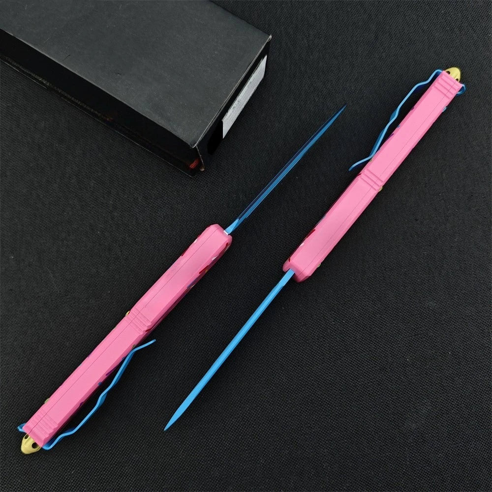 A pink tactical folding knife with a blue blade and aluminum handle lying on a black surface.