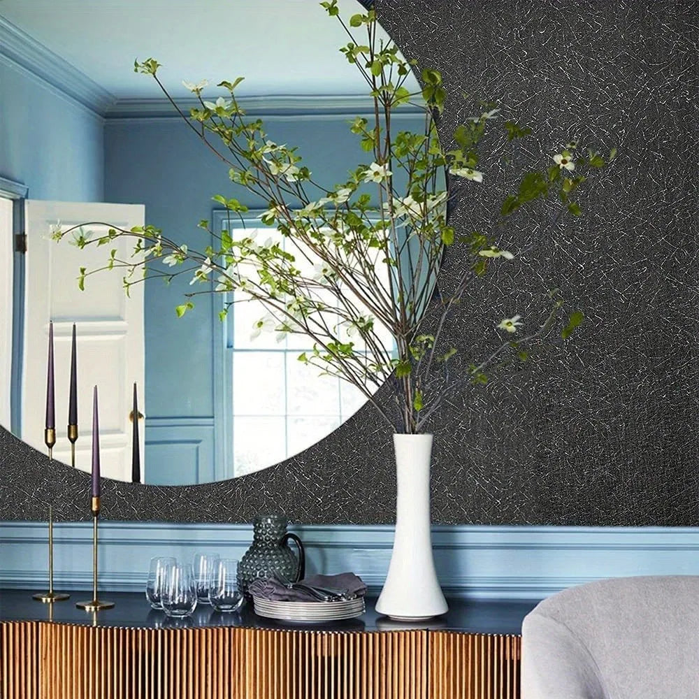 Jarrón decorativo con ramas verdes sobre una superficie oscura frente a una pared gris texturizada y zócal pintado de azul.