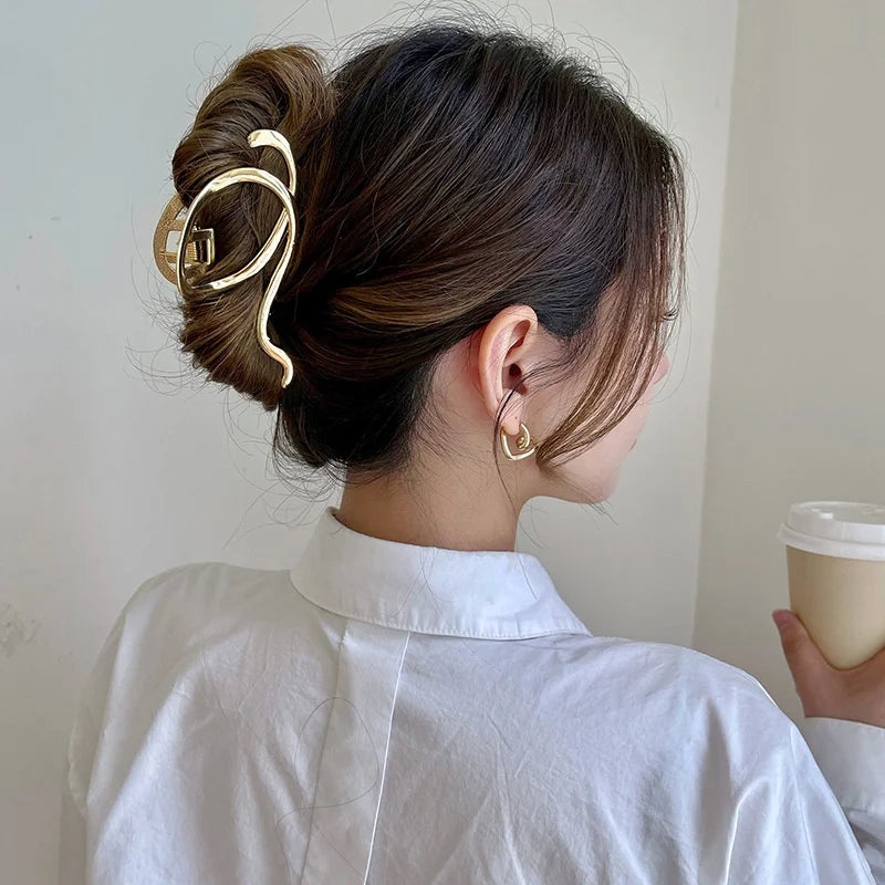 A woman with dark hair is shown from the side, wearing elegant gold S-shaped metal hair clips and a white collared shirt.
