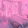 A bedroom decorated with pink fairy lights draped on curtains and a bed with a checkered blanket.