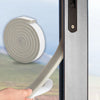 A hand is applying self-adhesive foam weather stripping tape to a window frame.