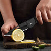 Une main tient un jeu de couteaux à fruits noirs avec un citron coupé sur une surface en bois.