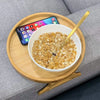 A bowl of rolled oats and a smartphone are displayed on a natural wooden tray.