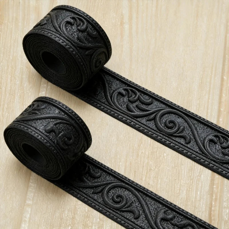 Black 3D embossed flexible foam wall trim molding rolls and strip on a light wooden surface