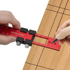 A hand uses a red precision aluminum woodworking ruler to mark a piece of wood.