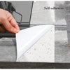 A hand applies a self-adhesive white marble sticker to a gray marble surface for home decor.