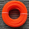 A coil of bright orange heavy duty lawn trimming line spools resting on a gray textured mat.