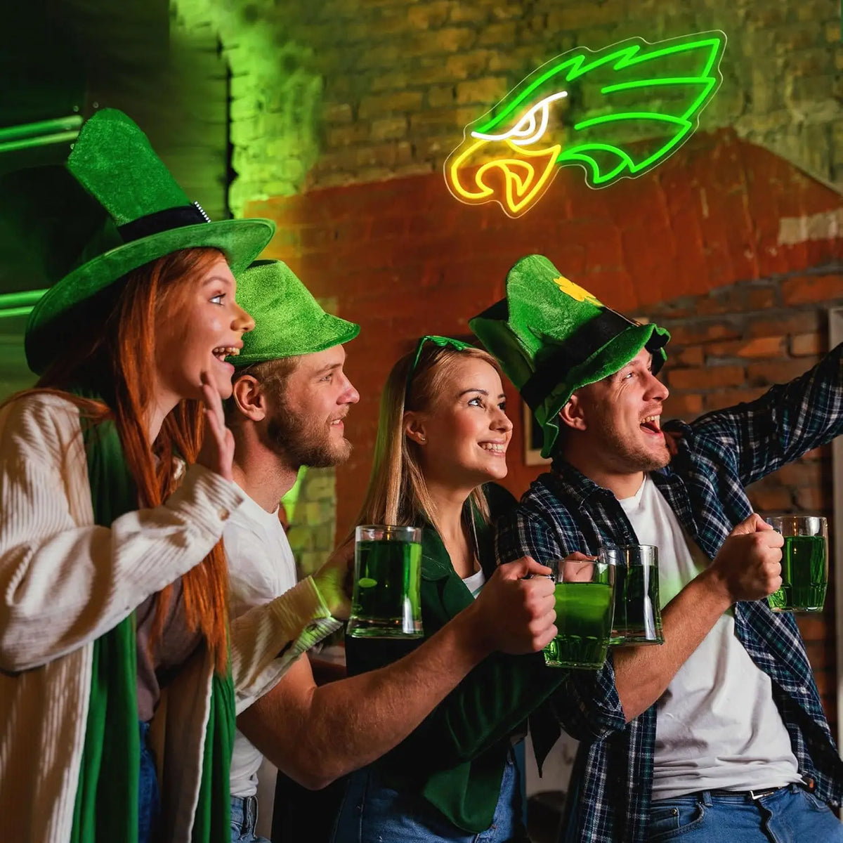 Four people cheering while holding green neon drinks in front of a brick wall background.