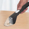 A hand holds a black handheld pest catcher with a clear glass-like tip, trapping an insect on a wooden surface.