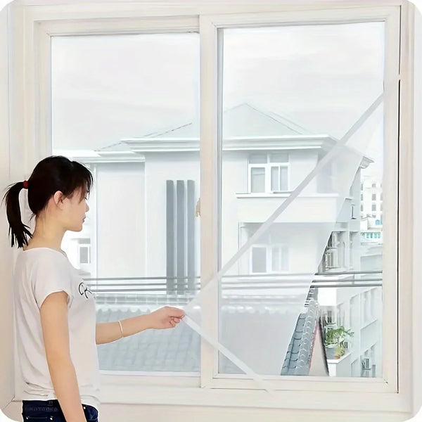 Eine Frau hält ein unsichtbares Moskitonetz vor ein großes Fenster mit Blick auf ein modernes Haus.