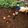 A hand is using a heavy-duty spiral garden auger drill bit to bore a hole in dark soil.