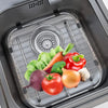 A premium stainless steel sink protector grid holds various fresh vegetables like tomatoes, peppers, and greens in a kitchen 