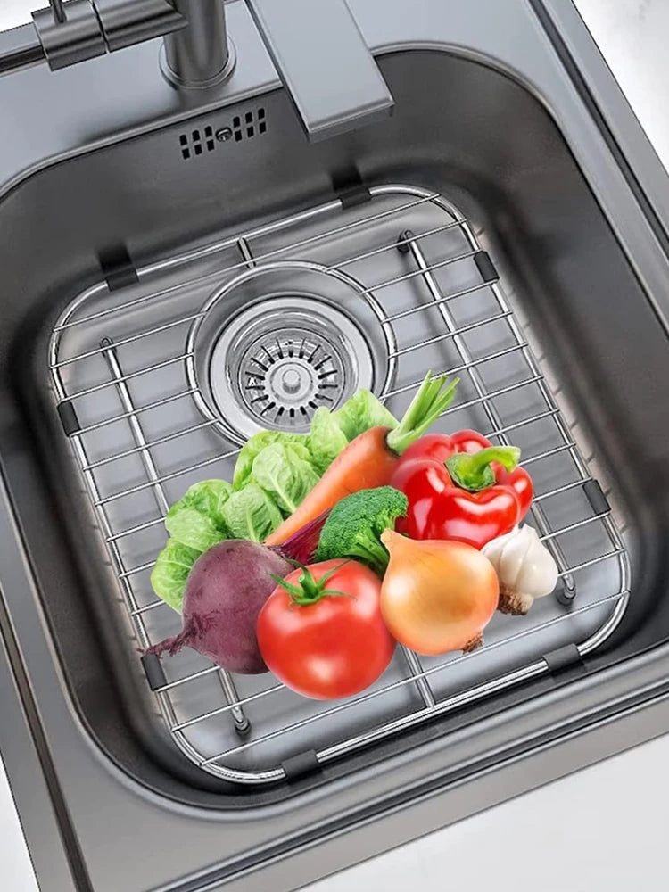 A premium stainless steel sink protector grid holds various fresh vegetables like tomatoes, peppers, and greens in a kitchen 