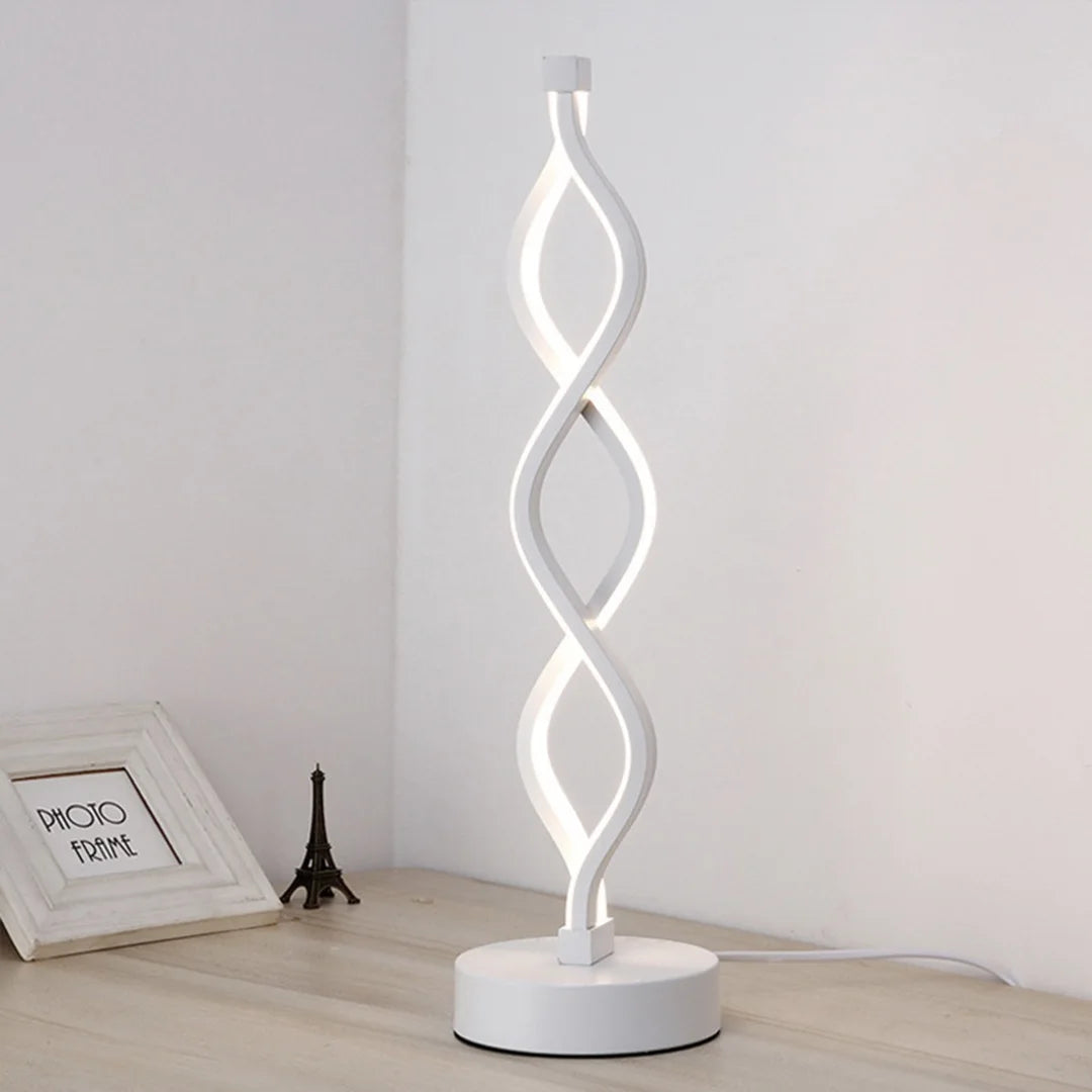 A white, wavy glass desk lamp with a modern design standing on a round base.