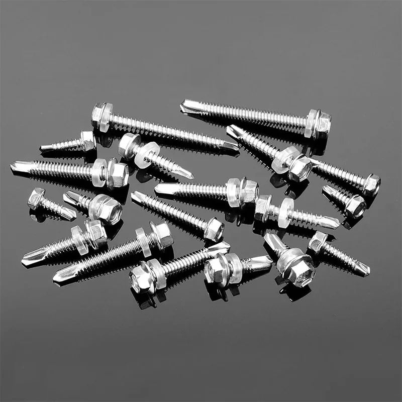 A collection of stainless steel self-drilling screws scattered on a dark gray surface.