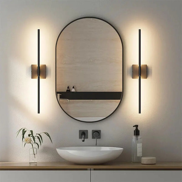 A round mirror above a white vessel sink is illuminated by modern wall sconces.