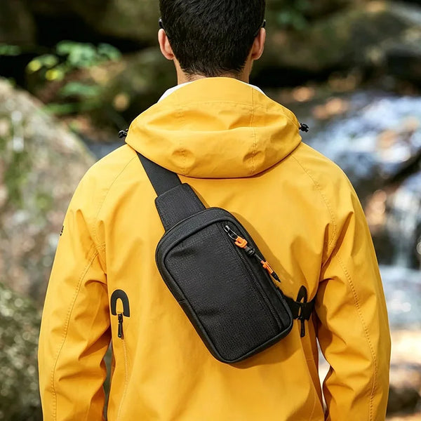 Ein Mann trägt eine gelbe Nylonjacke mit einer schwarzen Sling-Crossbody-Tasche auf dem Rücken.