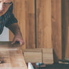 A man is using a multi-function oscillating cutting blade on a piece of wood in a workshop setting.
