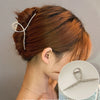 A close-up of a woman's hair styled in an elegant updo, featuring gold S-shaped metal hair clips.