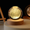 A glass crystal ball night light with a glowing yellow-green interior resting on a wooden base.
