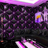 Interior moderno con pared geométrica negra y luz LED morada, junto a un sofá de cuero negro.