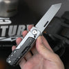 A hand holds a silver compact multi-tool pocket knife with a black handle and blade, displayed against a dark background.