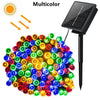 A cluster of multicolor solar powered outdoor LED string lights with a solar panel attached.