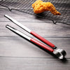 A pair of stainless steel BBQ grill tongs and kitchen clips resting on a dark wooden surface with a fried piece of food in th