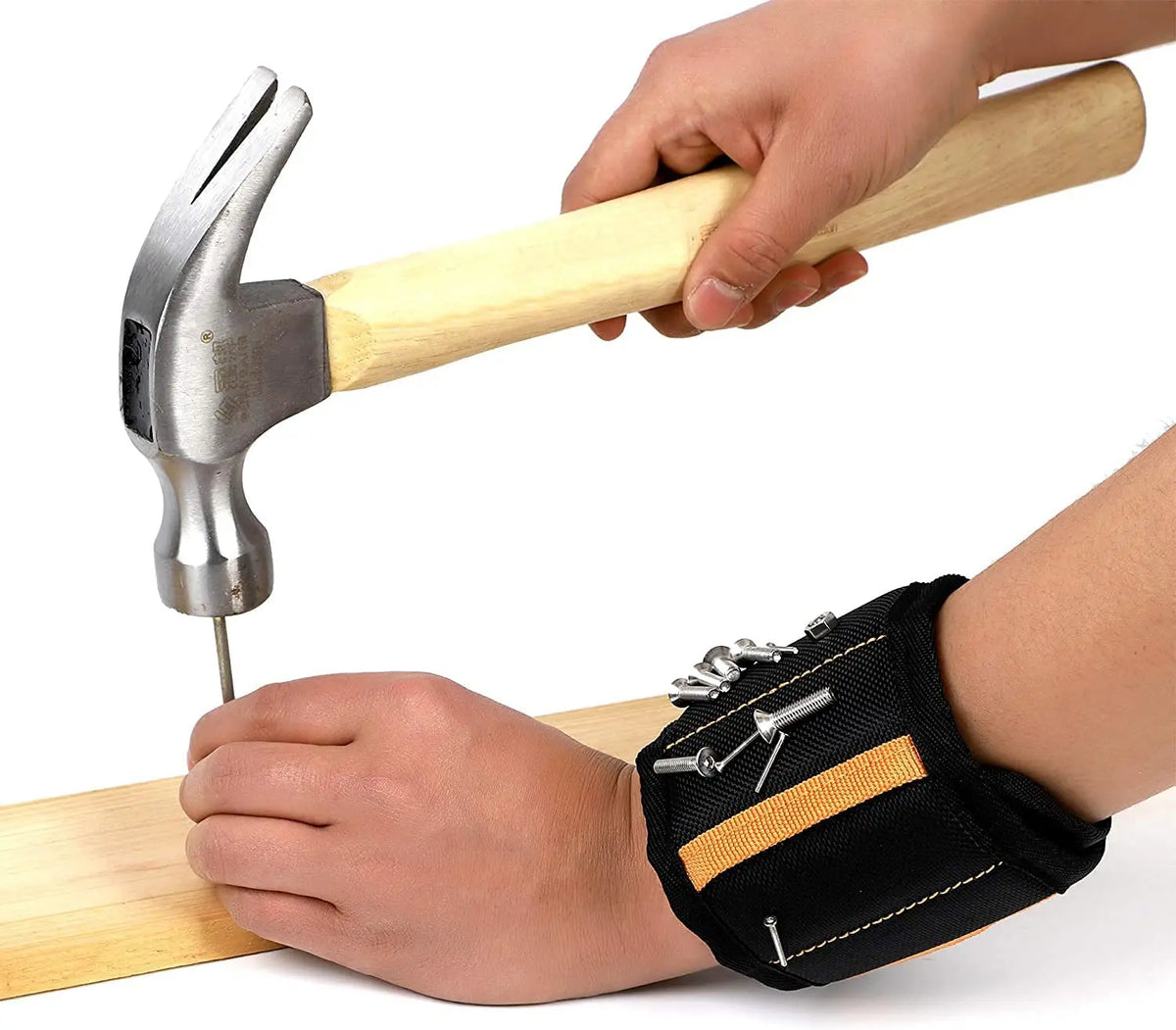 A hand uses a magnetic wrist strap tool with a wooden handle to drive a nail into a wooden board.