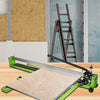 A manual tile cutter is shown on a wooden surface, cutting a piece of beige tile material.